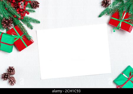 Mockup Christmas greeting card top view, flatlay Christmas fir branches, pine cones, gift boxes with red ribbon on a white paper background , space fo Stock Photo
