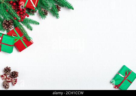 Christmas frame made of fir branches, festive decorations, gift boxes, red holly berries and pine cones on white table. Christmas background. Flat lay Stock Photo