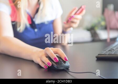 Closeup of hand businesswoman using mouse to working desktop and holding smartphone to connect online. Woman using computer mouse with pc on black tab Stock Photo