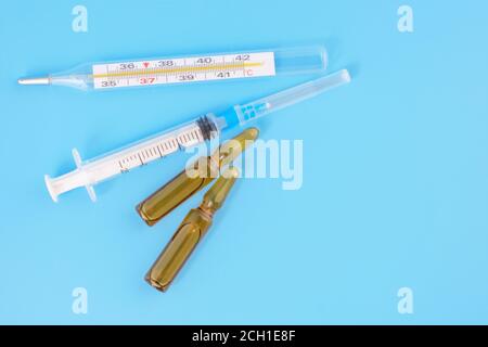 Medical ampoules, syringe and Medical mercury thermometer on blue background. Medical vial for injection with a syringe. Medical treatment concept. Stock Photo