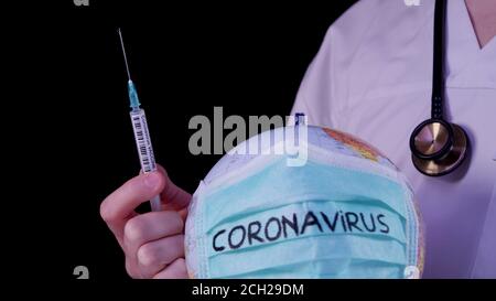 Coronavirus epidemic concept. World globus with green medical mask on it. Doctor holding syringe with COVID-19 vaccine.  World map, Wuhan virus Stock Photo