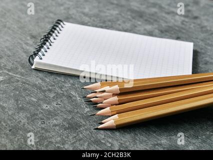 Notebook and stack of simple golden colored pencils on gray background, shallow depth of field Stock Photo