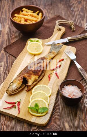 Fried sea bass with fried potato on wooden cutting board. Stock Photo