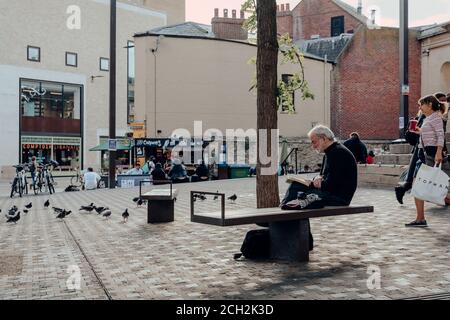Oxford, UK - August 04, 2020: Man reading a book sitting on a bench ona street in Oxford, a city in England famous for its prestigious university, est