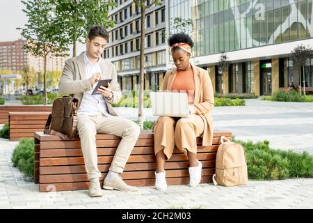 Two young contemporary intercultural co-workers using mobile gadgets Stock Photo