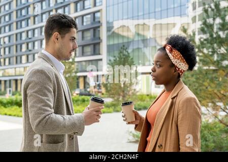 Two young multicultural colleagues in formalwear having drinks during discussion Stock Photo