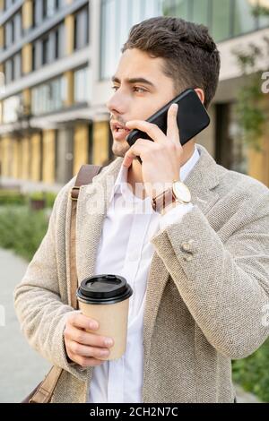 Young elegant man in white shirt and beige jacket having drink and phoning Stock Photo
