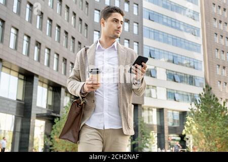 Busy young attractive manager with bag, drink and smartphone walking down street Stock Photo