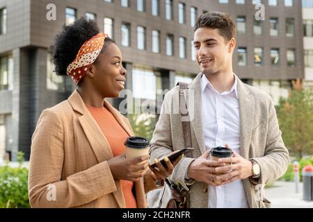 Cheerful African businesswoman with drink looking at colleague during promenade Stock Photo