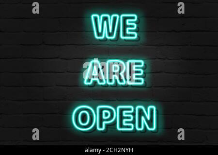 WE ARE OPEN - green neon light entrance sign on brick wall Stock Photo