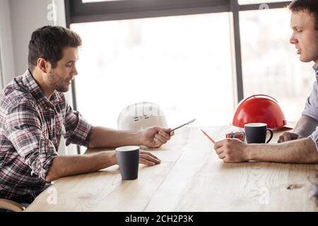 pensive builders holding a pen and a pencil while drinking tea at work. close up side view photo. break concept Stock Photo