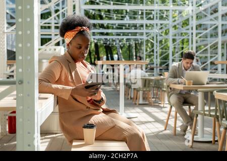 Young elegant woman of African ethnicity having drink and surfing in the net Stock Photo