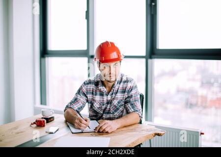 good loking young man wearing red hardhat is preparing business in the office with panorama window Stock Photo