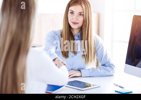 Business woman toned portrait while shaking hands with her female colleague or client in sunny office. Casual clothes style of business people. Audit Stock Photo