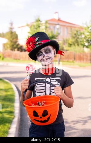 Cheerful boy with painted face in halloween t-shirt showing basket with sweets Stock Photo