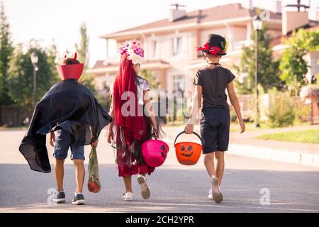 Back view of three halloween kids in costumes carrying baskets with treats