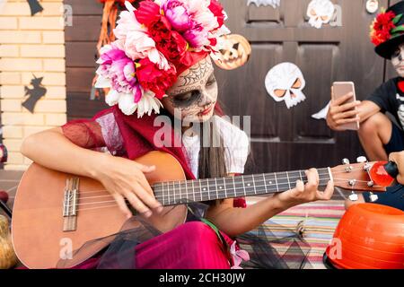 Cute little girl in halloween costume sitting on staircase and playing guitar