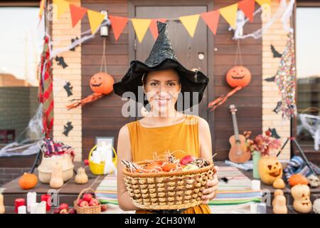 Young pretty woman in black hat of halloween witch holding basket with sweets Stock Photo