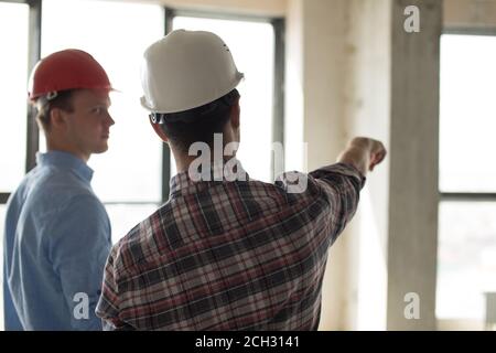 man in red hardhat is offering houses to a client. back view photo Stock Photo