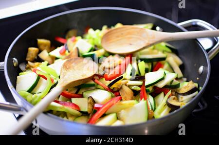 Stir fry fresh chopped eggplant, zucchini and peppers in the pan with wooden spoon. Preparing healthy food. Stock Photo
