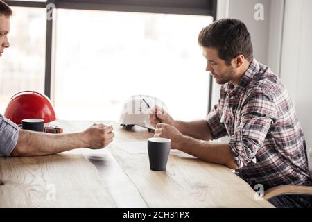 two handsome engineers are writing a plan of work while drinking coffee. close up side view shot Stock Photo