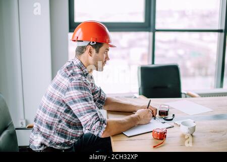 serious self-motivated builder is writing the plan of work in the notepad. side view close up portrait Stock Photo