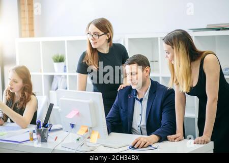 handsome chief sitting in front of computer and surrounding with beautiful women in the modern interior Stock Photo