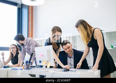 two young attractive women are standing and pointing to the document on the table. show mistakes in paper to co-worker Stock Photo