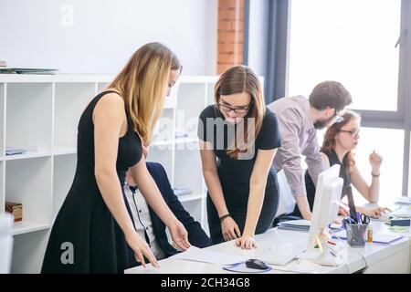 young female assiatants in black dresses are helping their chief with documents in the office with panorama window Stock Photo