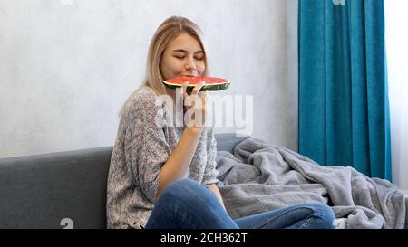 Young attractive woman bites a piece of watermelon. Woman at home in a cozy interior Stock Photo
