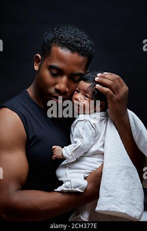 young Afro man trying to protect his insecure baby, protection concept. daddy takes care of his adorable baby. care and concern. close up portrait. is Stock Photo