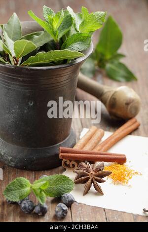 Anise, saffron, cinnamon, juniper berries and other spices in a vintage mortar on a rustic table Stock Photo