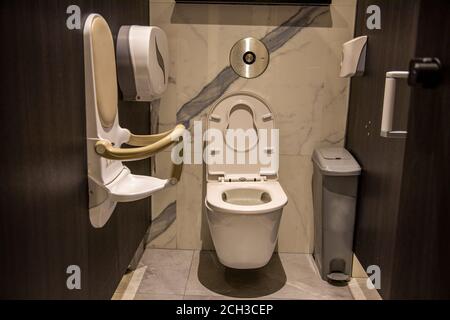 mother care publc toilet equipment. cubicle of a public toilet equipped Folding toddler safety chair mounted on wall in public restroom. friendly to Stock Photo