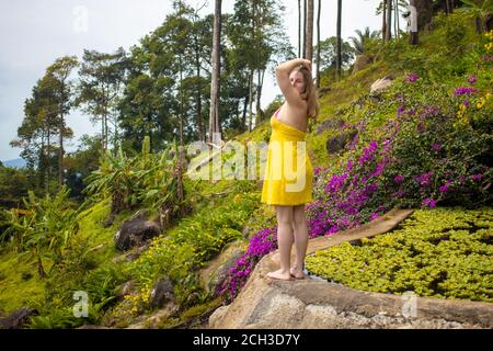 a young woman in a dress stands on the edge of a pond with water lilies and turns around against the backdrop of the tropics Stock Photo