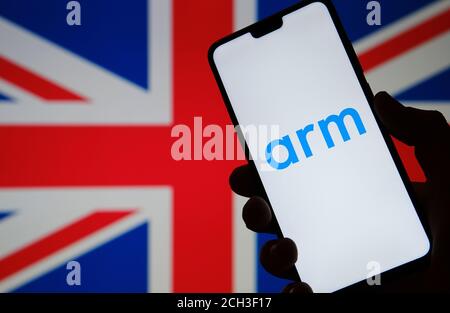 ARM Holdings logo seen on the silhouette of smartphone hold in hand and the United Kingdom flag on a blurred background Stock Photo