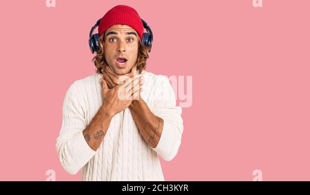 Young hispanic man listening to music using headphones shouting and suffocate because painful strangle. health problem. asphyxiate and suicide concept Stock Photo