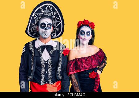 Young couple wearing mexican day of the dead costume over background making fish face with lips, crazy and comical gesture. funny expression. Stock Photo
