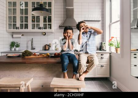 Two young boys making funny faces while in the kitchen with lunch