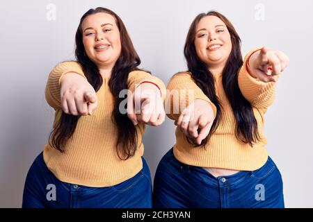 Young plus size twins wearing casual clothes pointing to you and the camera with fingers, smiling positive and cheerful Stock Photo