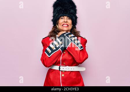 Middle age beautiful wales guard woman wearing traditional uniform over pink background shouting and suffocate because painful strangle. Health proble Stock Photo