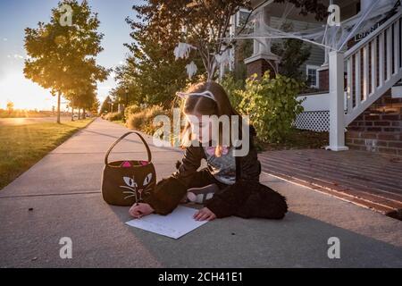 A young girl in a cat costume writes a note to the toothless fairy Stock Photo