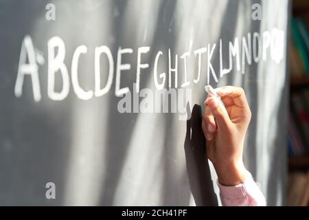 Hand of school girl pupil holding chalk writing english letters on blackboard. Stock Photo