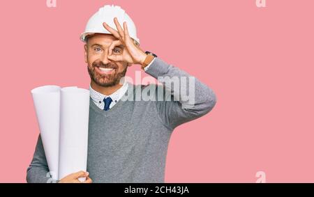 Handsome middle age man holding paper blueprints smiling happy doing ok sign with hand on eye looking through fingers Stock Photo
