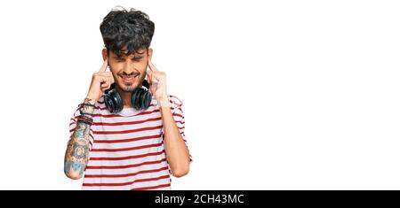 Young hispanic man listening to music using headphones covering ears with fingers with annoyed expression for the noise of loud music. deaf concept. Stock Photo