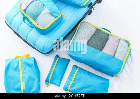 Suitcase and set of travel organizers with belongings on bed at home Stock Photo
