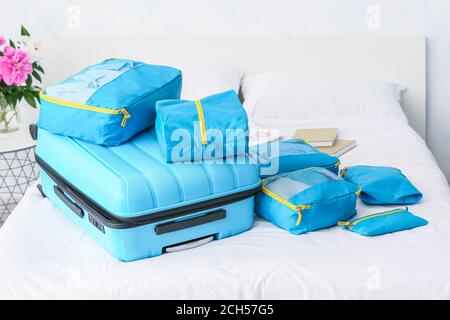 Suitcase and set of travel organizers with belongings on bed at home Stock Photo