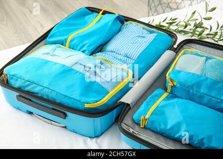 Suitcase and set of travel organizers with belongings on bed at home Stock Photo