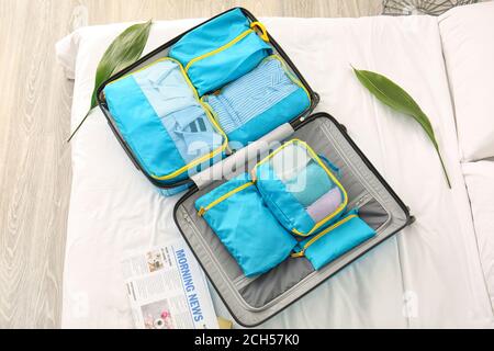 Suitcase and set of travel organizers with belongings on bed at home Stock Photo