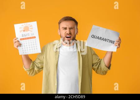 Angry man holding calendar and paper with written word QUARANTINE against color background Stock Photo