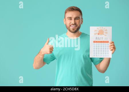 Young man with calendar showing thumb-up gesture on color background. Vacation concept Stock Photo